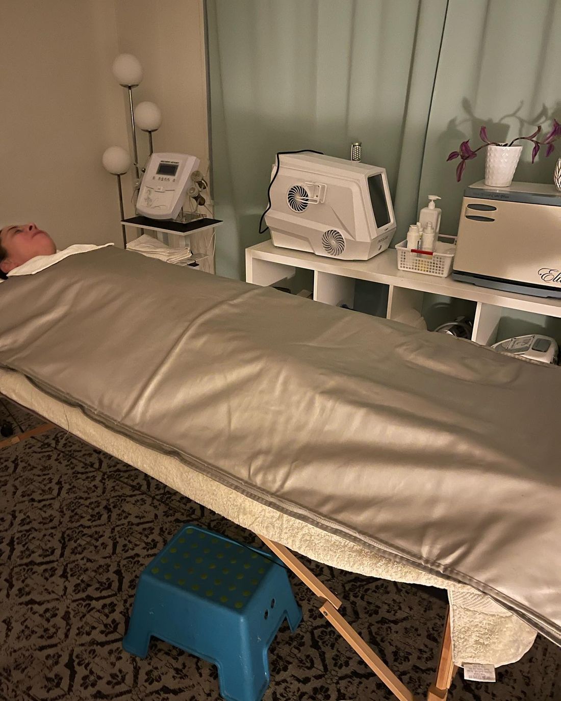 Elena's treatment room with a massage bed, an infrared sauna blanket and facial devices